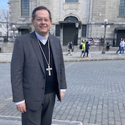 Un homme avec une croix autour du cou debout devant la Basilique Notre-Dame de Québec.