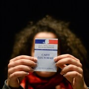 Une femme montre sa carte électorale, en France. On peut y lire : « Liberté, égalité, fraternité. La République française ».