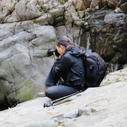 La photographe Catherine Babault assise sur un rocher est en train de prendre un cliché.