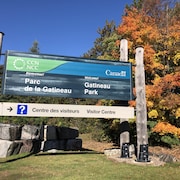 Affiche de la CCN à une des entrées du parc. Derrière des arbres aux feuilles jaunes et oranges.