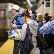Une femme tient un téléphone dans ses mains sur une plateforme du métro de Toronto.