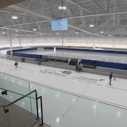 Vue sur une large piste de patinage de vitesse flambant neuve. Des patineurs glissent dessus.

