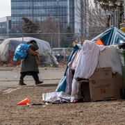 Une personne traîne un sac de cannettes sur son dos devant un abri de fortune.