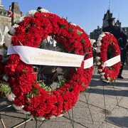 Trois couronnes de fleurs entourées chacune d'un ruban blanc avec une inscription de couleur or, placées devant le Parlement. Sur celle du centre, il est écrit « L'Association canadienne des policiers ».
