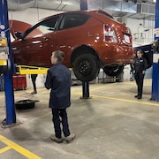 Des jeunes mécaniciens dans un garage avec une voiture surélevée.