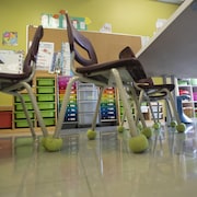 Des chaises avec des balles de tennis autour des pattes dans une classe d'école.