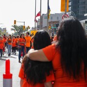 Des gens défilent dans la rue vêtues de chandails oranges. 
