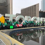Des personnes portant des vêtements verts posent devant l'hôtel de Ville de Toronto.