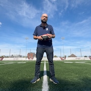 Un journaliste sur un terrain de football, tenant un ballon.