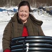 Une femme habillée en hiver tient un tuyau enroulé. Derrière se trouvent des centaines de tubulures dans un champ.