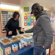 Chantal Rouillier sert un muffin à un autre élève. Des jus et des muffins sont disposés sur une table.