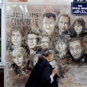 Une femme passe devant une murale reproduisant les visages de 10 employés de Charlie Hebdo.