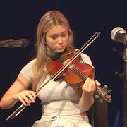 Une adolescente assise joue du violon.