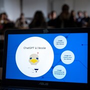 Un ordinateur portable ouvert pendant une séance de formation dans une classe. Sur l'écran, on voit un dessin de tête d'autruche circonspect avec au-dessus de sa tête les mots : ChatGPT à l'école.