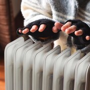 Une femme place ses deux couvertes de gants aux doigts coupés au-dessus d'un radiateur dans un appartement.