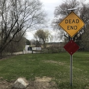 Des pancartes annonçant une route barrée, avec les indications « Road closed » et « Dead end », plantées sur un terrain devant une barrière qui bloque une route.
