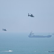 Des hélicoptères volent au-dessus de la mer, où se trouvent des navires.