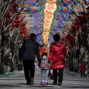 Un couple, de dos, tient par les bras un enfant, de face, dans une allée décorée à l'occasion du Nouvel An chinois, à Pékin.