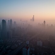 Une ville dont les bâtiments sont embrumés en raison de la pollution est vue de haut et de loin lors du lever du soleil.