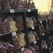 Deux clients de dos qui choisissent une figurine de Pâques en chocolat dans un commerce.