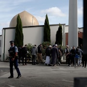 Un policier armé devant quelques fidèles à l'extérieur d'une mosquée.
