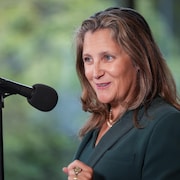 Chrystia Freeland parle dans un micro et sourit.