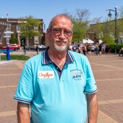 Un homme debout à l'extérieur regarde la caméra. 
