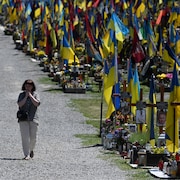 Une femme marche au milieu de tombes et de drapeaux ukrainiens.