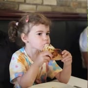 Montage photos montrant d'un côté la petite Claire Bell en train de manger une pointe de pizza et de l'autre, à genoux en train de dessiner sur un tableau.
