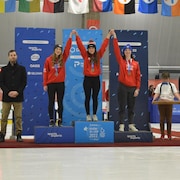 Trois jeunes filles sur un podium lèvent les bras. 