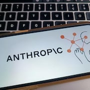 Un téléphone cellulaire avec comme image le logo d'Anthropic est posé sur un clavier d'ordinateur. 