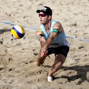 Un joueur qui se penche pour frapper un ballon de volleyball sur une plage lors d'une rencontre.