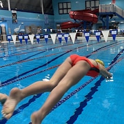 Une jeune femme est photographiée dans les airs alors qu'elle plonge dans une piscine pour une course.