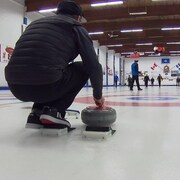Un joueur de curling s’apprête à lancer une pierre.