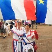 Deux femmes costumées brandissent des drapeaux de l'Acadie.