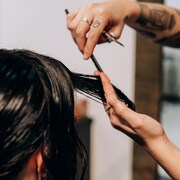 Une coiffeuse coupe les cheveux d'une cliente à l'aide de ciseaux. 
