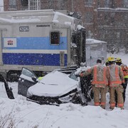 Une voiture emboutie par un train entourée de pompiers et secouristes.