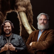 Les cofondateurs de Colossal : Ben Lamm et George Church prennent la pose devant une illustration de mammouth laineux.