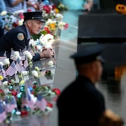 Un homme en uniforme regarde le site où était autrefois le World Trade Center, entouré de fleurs et de drapeaux américains.