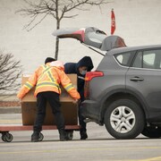 Un employé de quincaillerie aide un homme à mettre une boîte dans le coffre de sa voiture dans un stationnement.