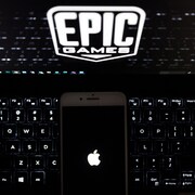 Le logo d'Apple affiché sur un téléphone, qui est déposé sur un clavier d'ordinateur dont l'écran affiche le logo d'Epic Games.