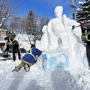 Des gens s'affairent à sculpter un bloc de neige où une forme humain prends tranquillement forme.
