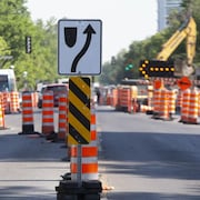 Des cônes orange et des pancartes de signalisation de travaux de construction font dévier la circulation dans une rue.