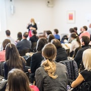 Une conférencière fait une présentation devant une foule de quelques dizaines de participants.