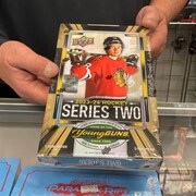 Le copropriétaire du magasin de cartes de collection The Nutman Cards and Collectibles à Regina, Tanner Piper, tient une boîte contenant des paquets d'un nouveau jeu de cartes de hockey, qui contient la carte de recrue Young Guns de Connor Bedard.