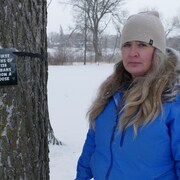 Rebecca Rummery devant un panneau attaché à un arbre et expliquant que 138 Manitobains sont morts de surdoses durant les six premiers mois de 2020.