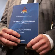 Des mains tenant un exemplaire de la Constitution canadienne.