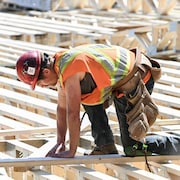 Un travailleur en construction est accroupi sur des planches de bois qui formeront un toit ou un plancher d'une bâtisse.