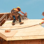 Deux travailleurs sur le toit d'une maison en cours de construction.