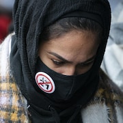 Une femme porte un couvre-visage sur lequel est épinglé un macaron contre la loi 21.